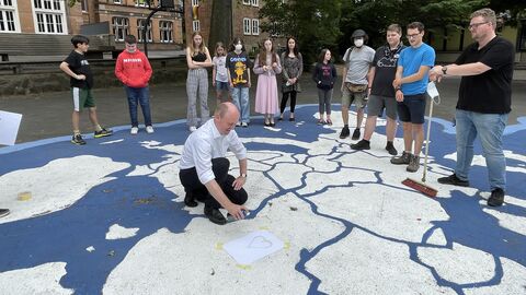EU-Projekttag 2022 an der Albert-Schweitzer-Schule Kassel Europastaatssekretär Uwe Becker beim Sprühen der Farben auf der EU-Karten am Asphalt