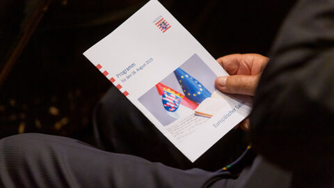 Ein Gast hält das Programm des Abend in der rechten Hand