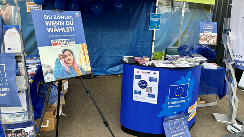 Informationen zur Europawahl 2024 Es ist das Innere eines Infostandes zur Europawahl zu sehen. Es gibt Plakate, Flaggen, Flyer und weiteres Informationsmaterial.