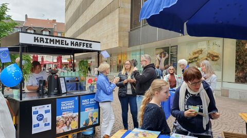 Bürgerinnen und Bürger beim Kaffee am Infostand Zwischen dem Kaffee-Mobil und einem Informationsstand sind Menschen ins Gespräch vertieft.