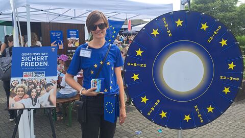 Europa bringt Glück! Eine Mitarbeiterin der Staatskanzlei steht mit EU-T-Shirt neben dem EU-Glücksrad und blickt in die Kamera.