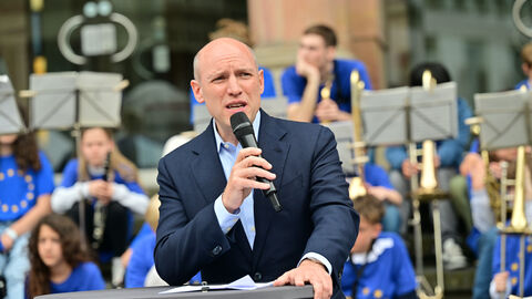 Rede von Europaminister Manfred Pentz Europaminister Manfred Pentz hält eine Rede an einem Stehtisch auf der Bühne vor dem Rathaus. Im Hintergrund ist die Band der Diltheyschule auf den Stufen des Rathauses zu sehen.